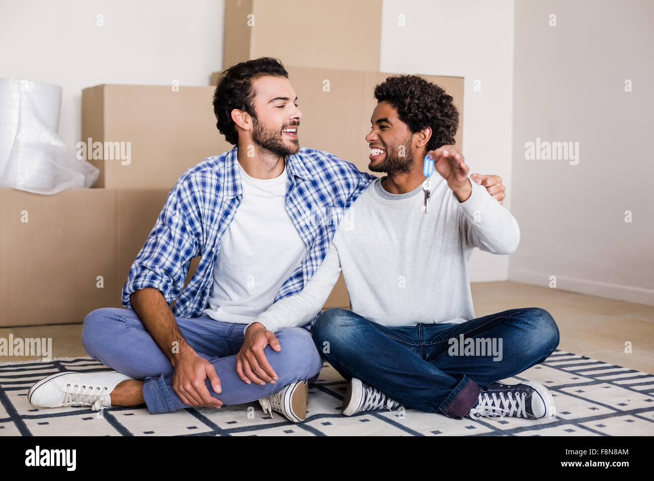 Happy gay couple holding nouvelles clés de maison sitting on floor Banque D'Images
