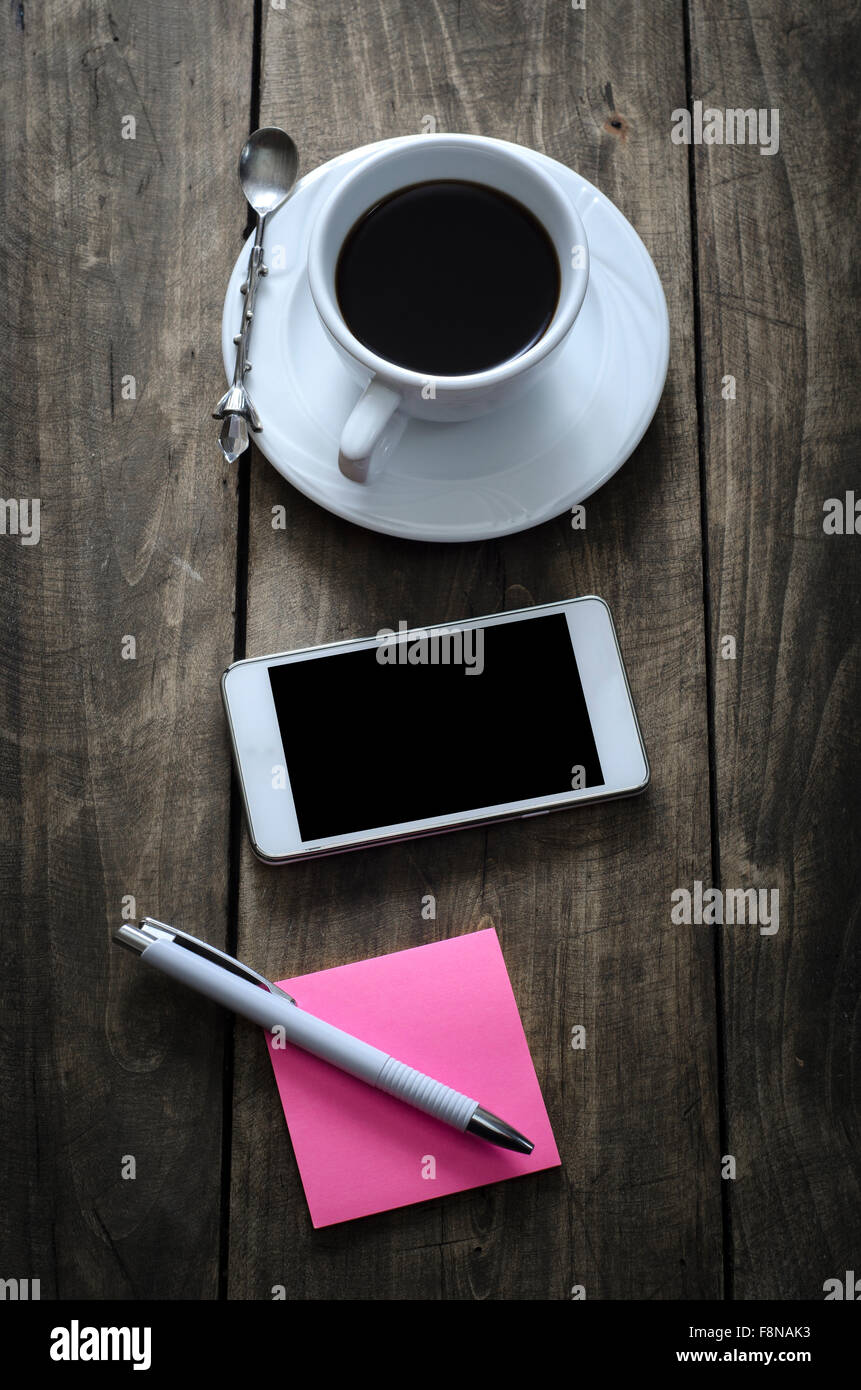 Téléphone avec sticky note papier et tasse de café sur le vieux bureau en bois. Banque D'Images