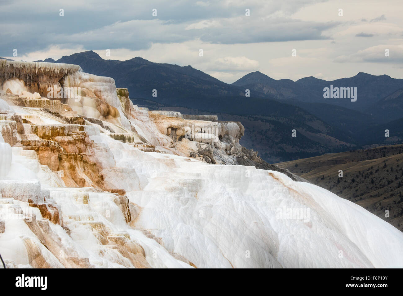 Le flux géothermique de chaud, l'eau riche en carbonate, formulaires, en cascade de terrasses en travertin orange foncé, avec des montagnes en arrière-plan Banque D'Images
