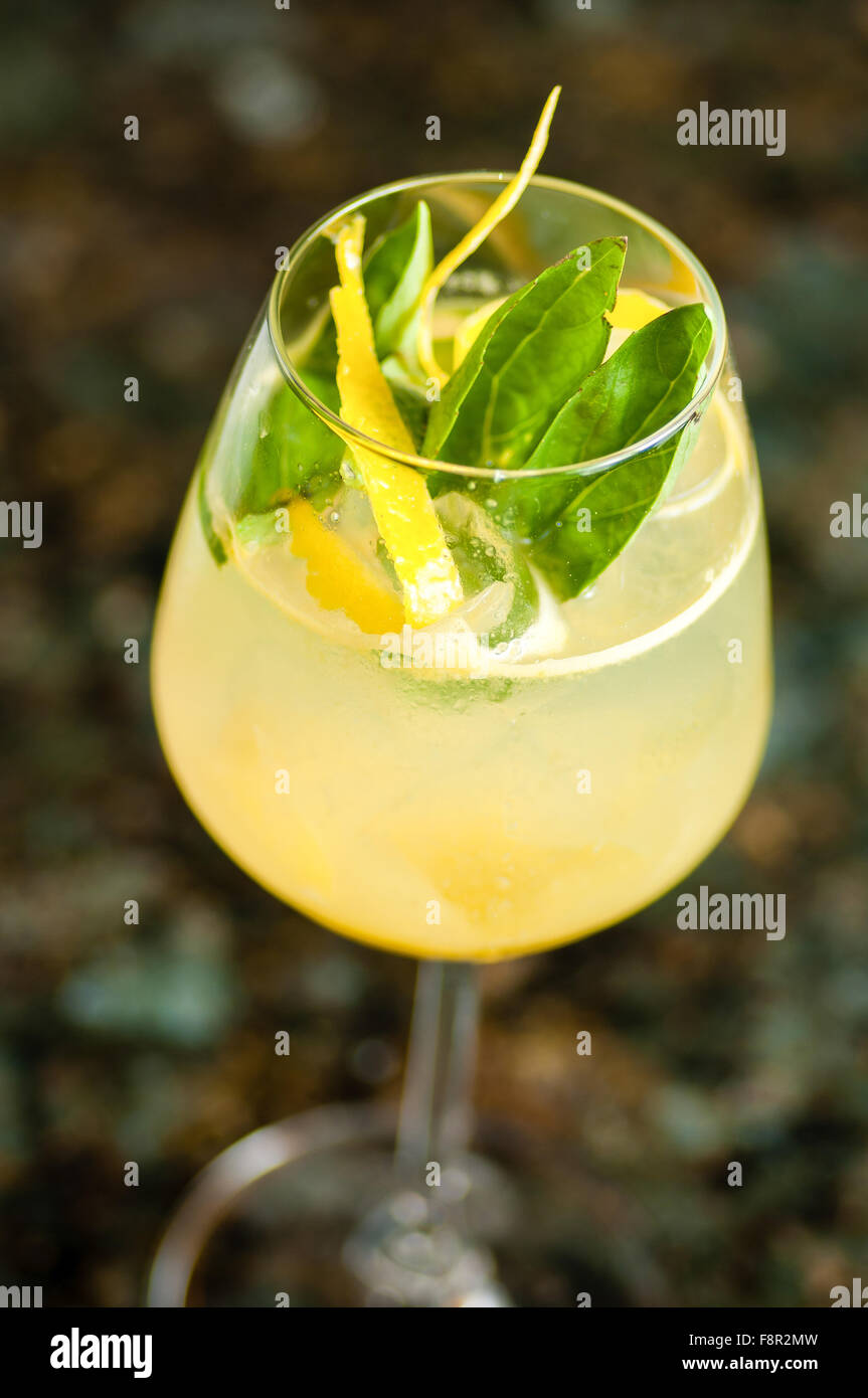 Close-up d'un verre de vin misty rempli de liquide semi-transparent jaune, décoré avec des feuilles vertes et ruban-comme le citron ze Banque D'Images