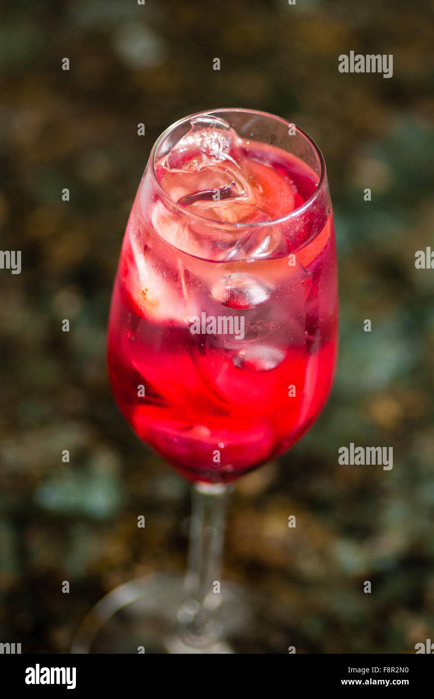 Close-up d'une flûte de champagne misty rempli de liquide rouge et des cubes de glace, sur un arrière-plan flou et laisse la terre Banque D'Images