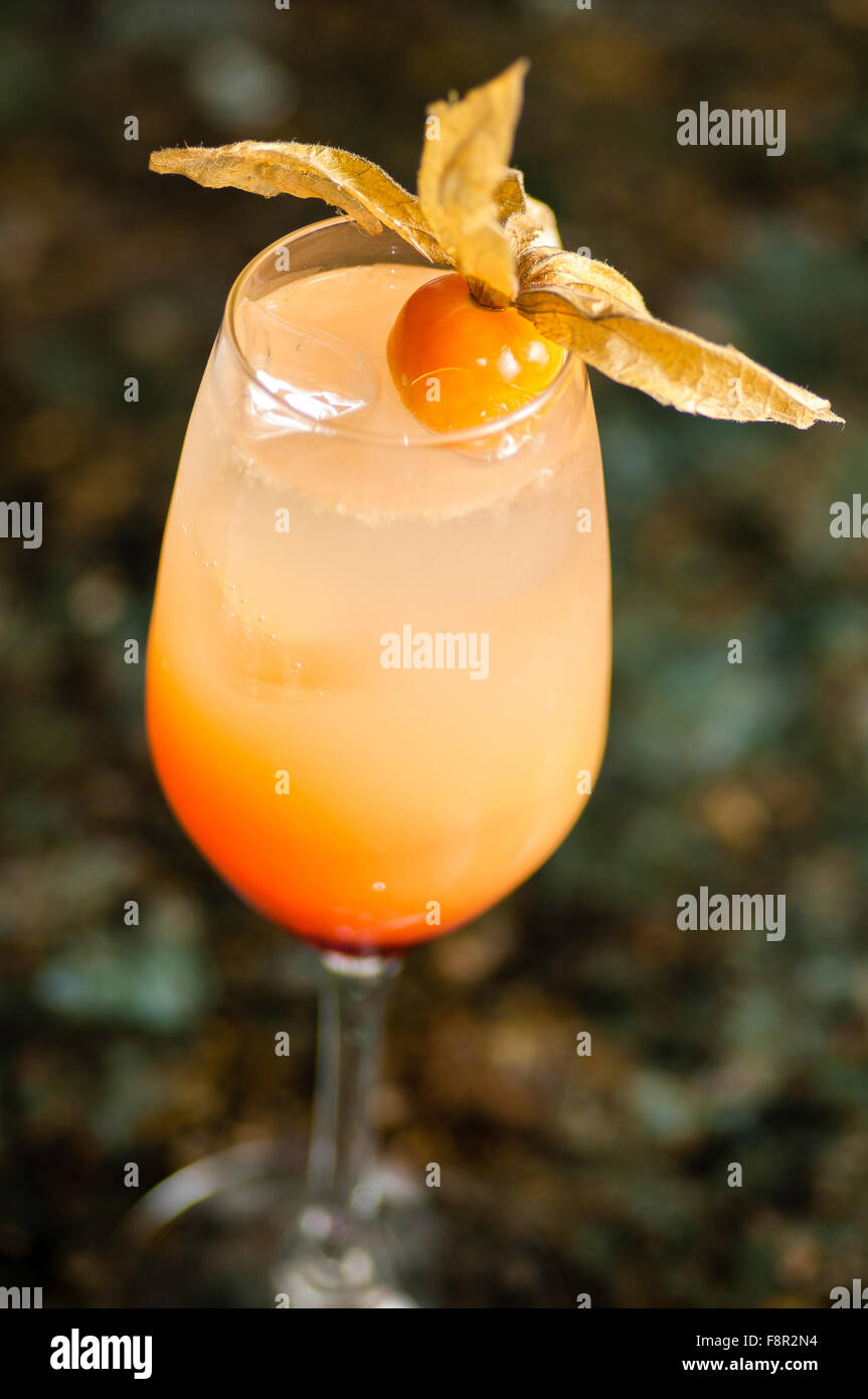Close-up d'une flûte de champagne misty rempli de liquide opaque dégradé orange et de la glace, décoré d'une physalis les fruits, sur un b Banque D'Images