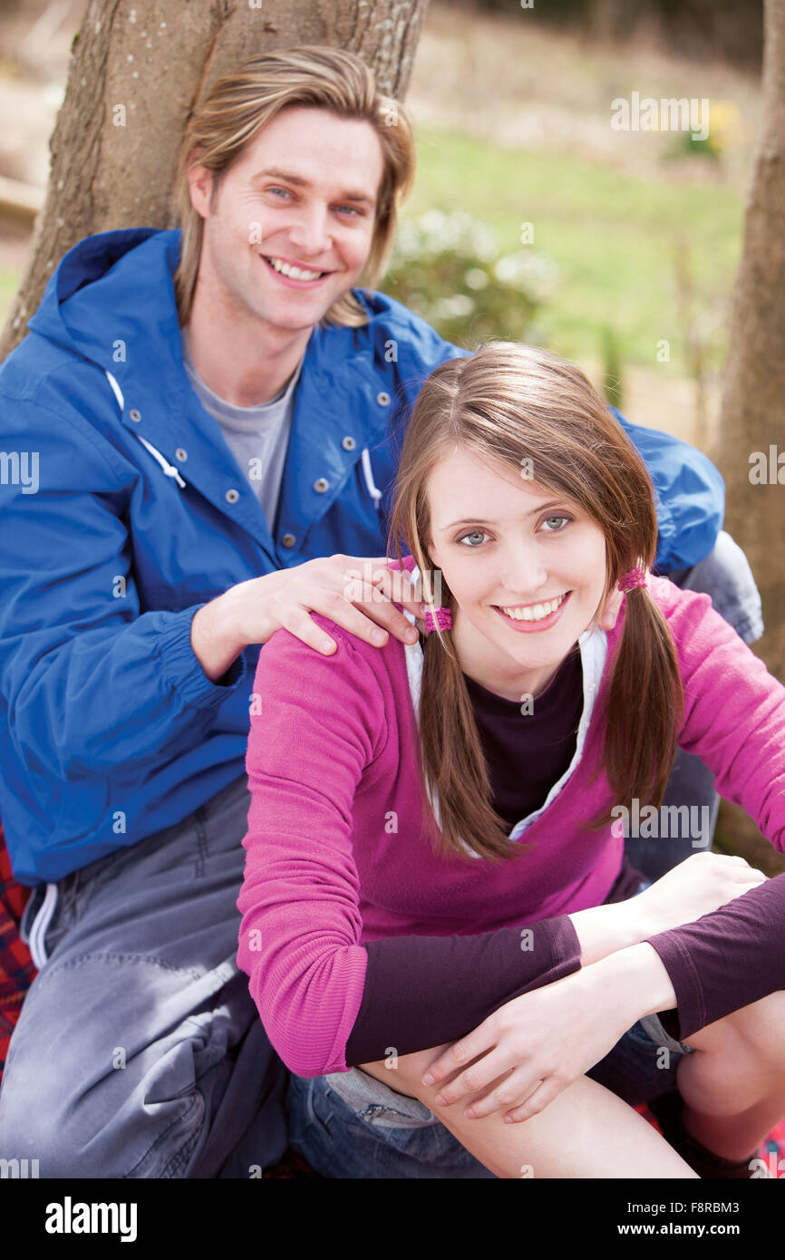 Jeune couple assis sur un tronc d'arbre à l'extérieur, smiling at the camera Banque D'Images