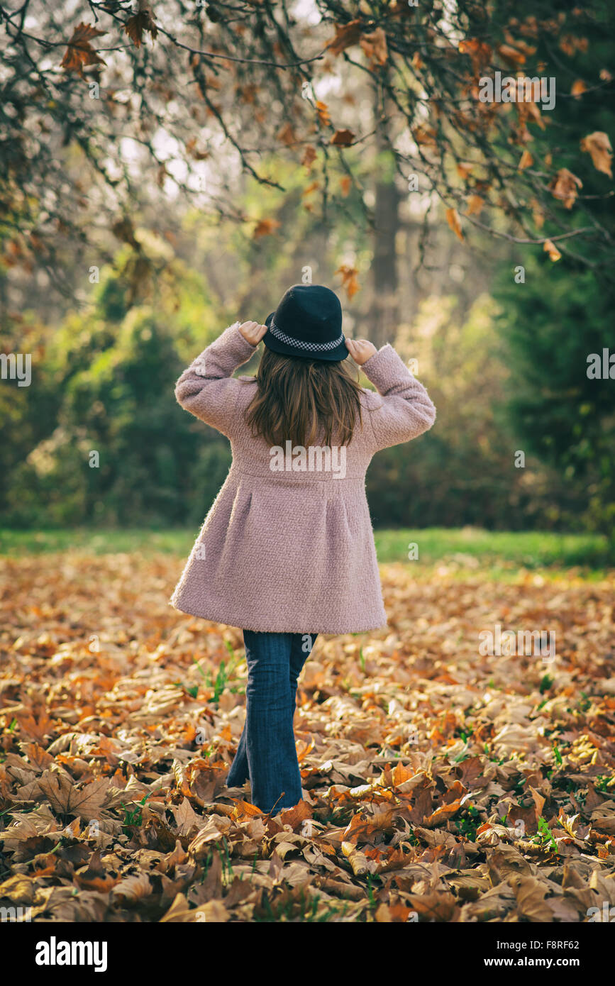 Vue arrière d'une jeune fille debout dans les feuilles d'automne Banque D'Images