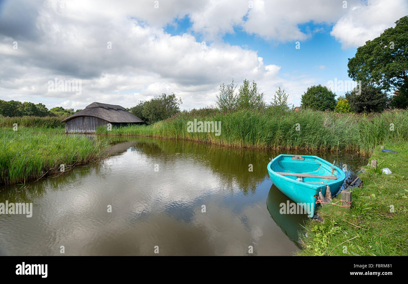 Un aviron turquoise bateau amarré à l'extérieur d'un hangar à chaume traditionnel sur le large Hickling Norfolk Broads Banque D'Images