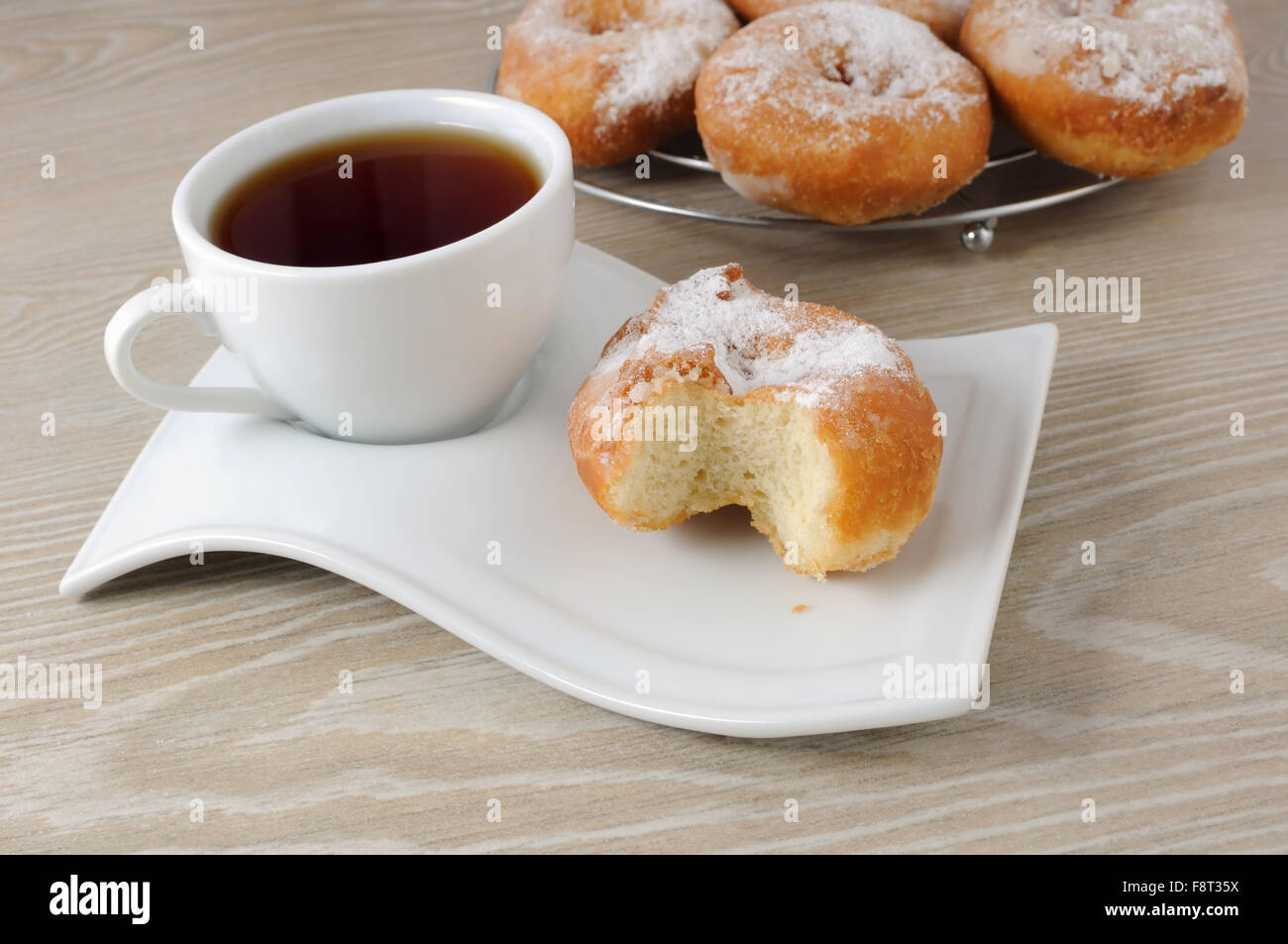 Une tasse de café et beigne mordu dans le sucre en poudre sur une assiette Banque D'Images