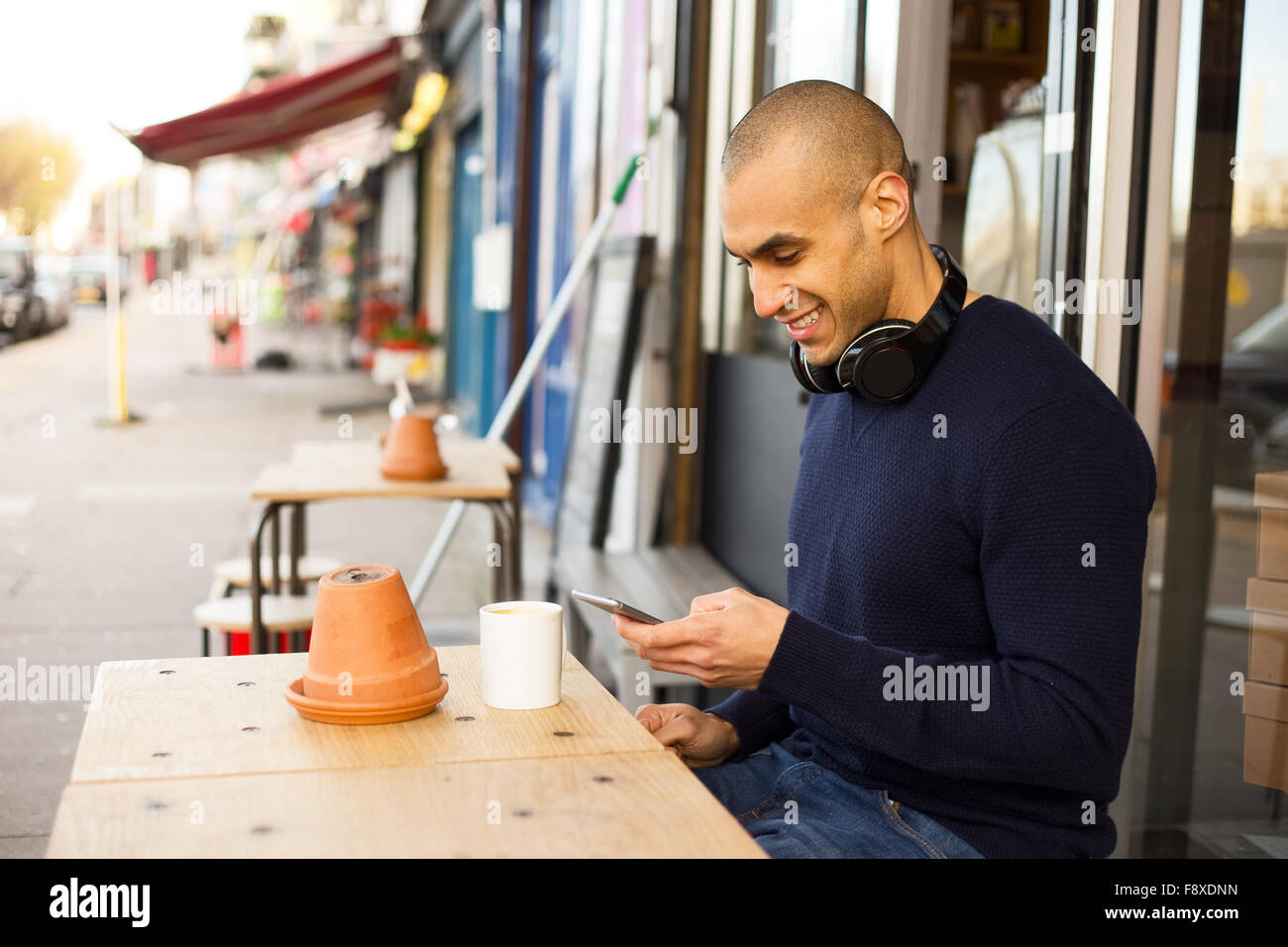 Jeune homme assis à l'extérieur d'un café en utilisant son téléphone Banque D'Images