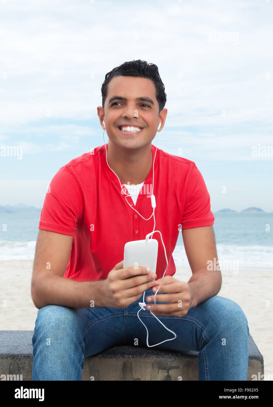 L'gars en chemise rouge à l'écoute de la musique avec phone at beach Banque D'Images