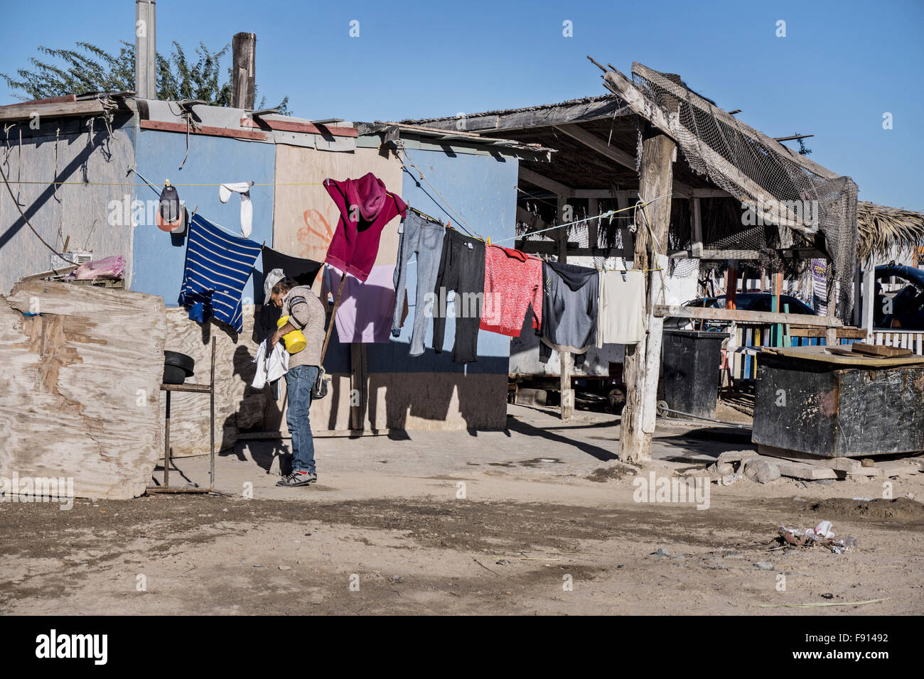 Vieille Femme portant des jeans & argent baseball cap rassemble de charge blanchisserie séchées au soleil à l'extérieur dans un abri simple vieux port Puerto Penasco Banque D'Images