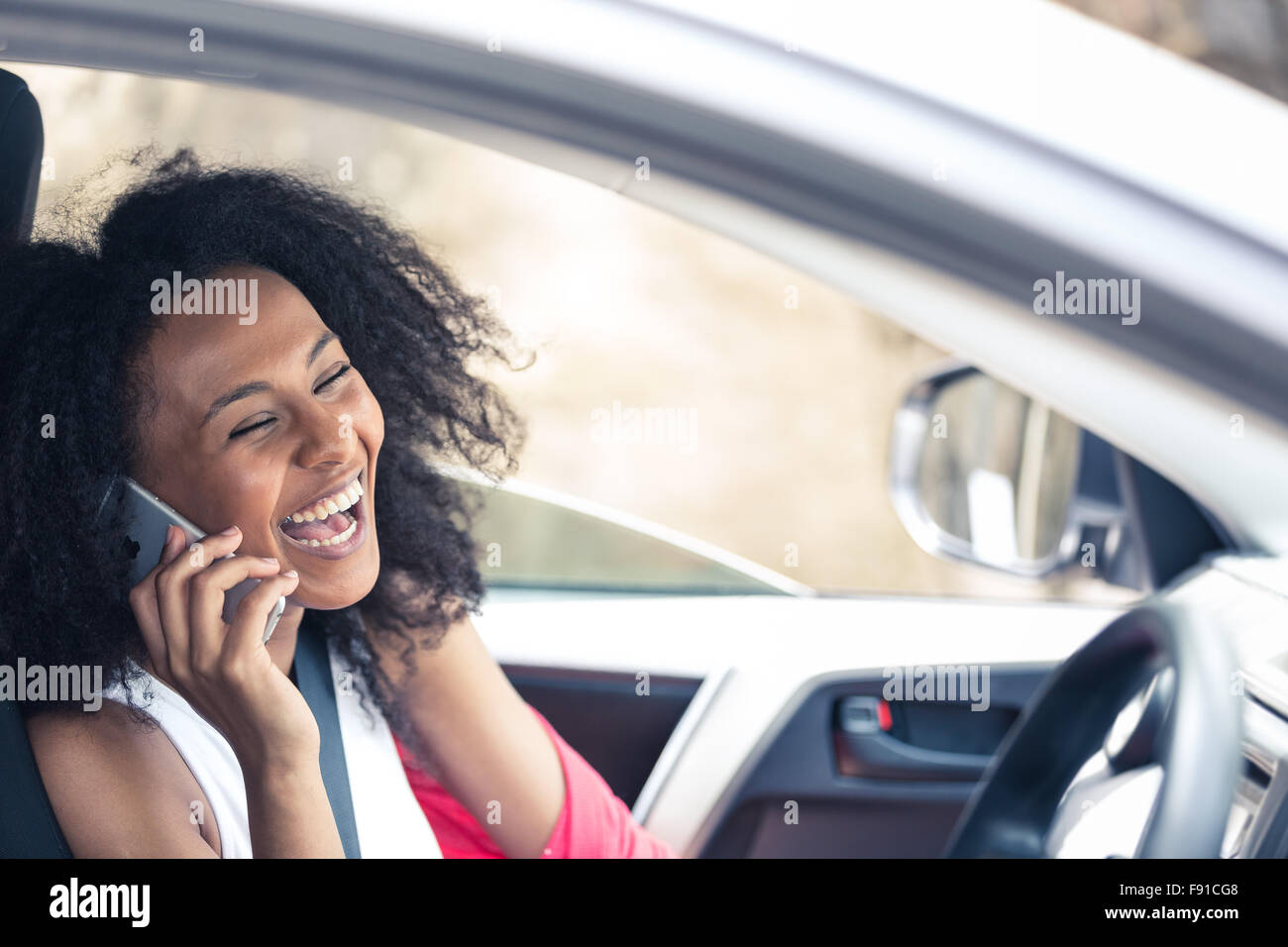 Une jolie jeune femme métisse dans une voiture sur son téléphone mobile comme un passager Banque D'Images