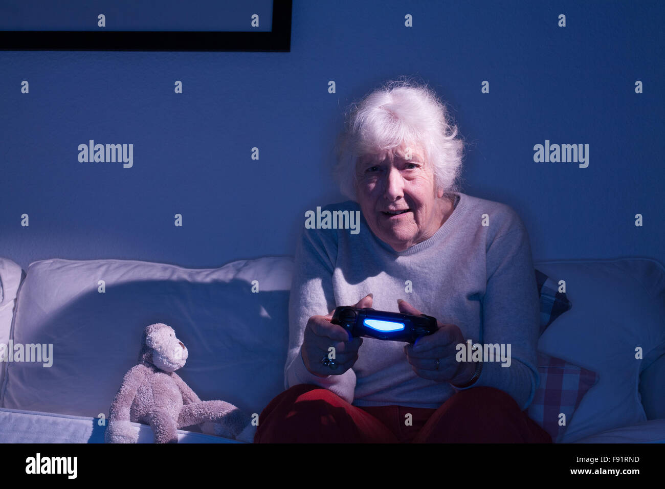 Vieille dame assise sur un canapé se concentrant tout en jouant sur une Playstation 4 à côté d'un singe en peluche. Banque D'Images