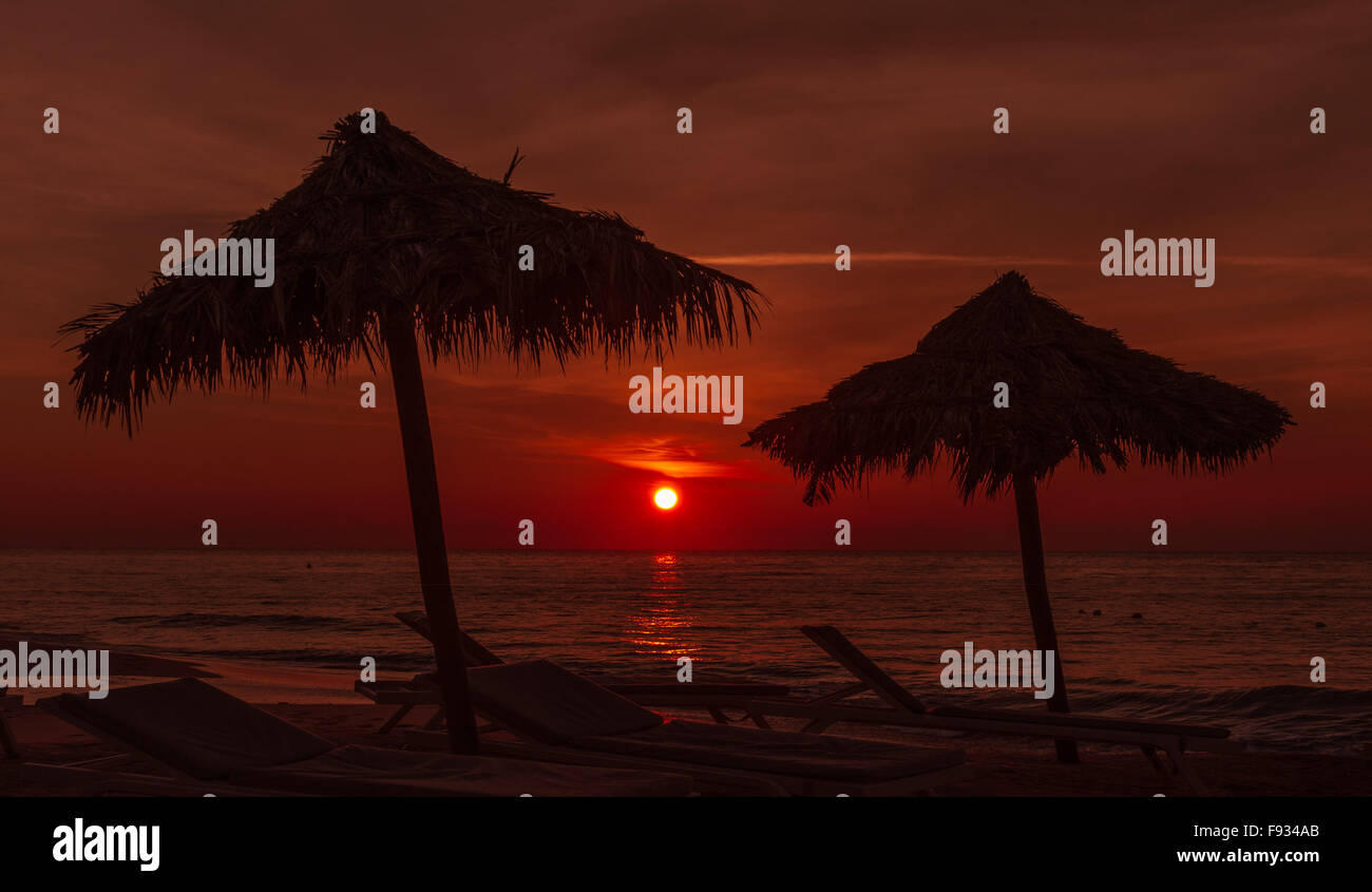 Coucher du soleil à la plage avec des parapluies et quelques chaises au premier plan, le coucher de soleil dans la distance Banque D'Images