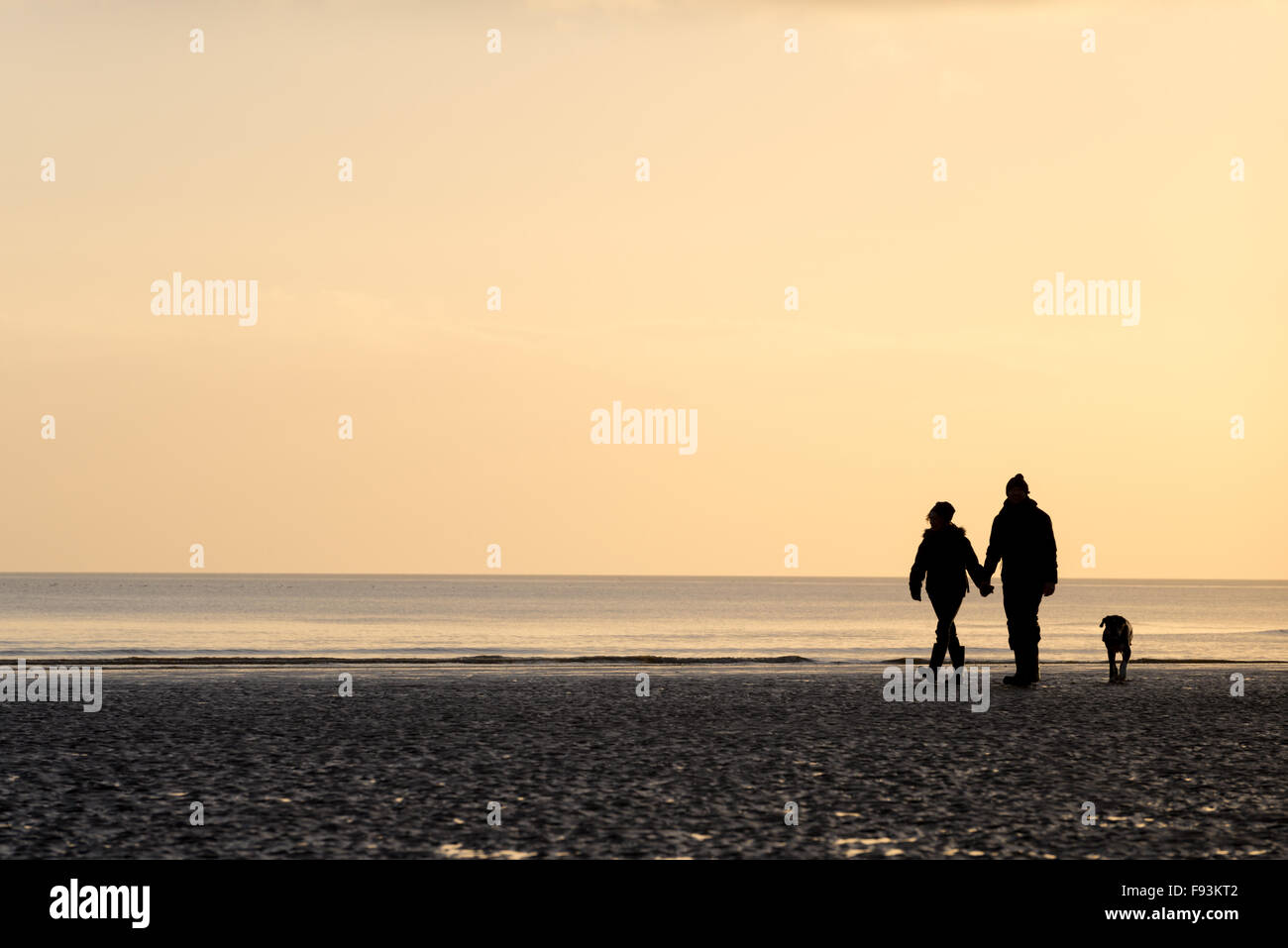 Un couple en train de marcher leur chien et tenir la main sur la plage de Camber, East Sussex. Banque D'Images