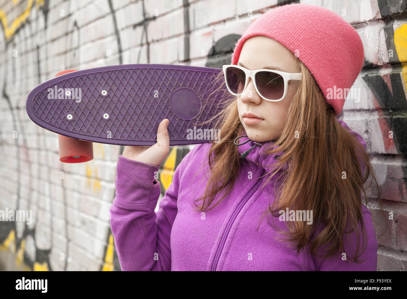 Teenage girl détient près de skateboard en milieu urbain mur de graffiti Banque D'Images