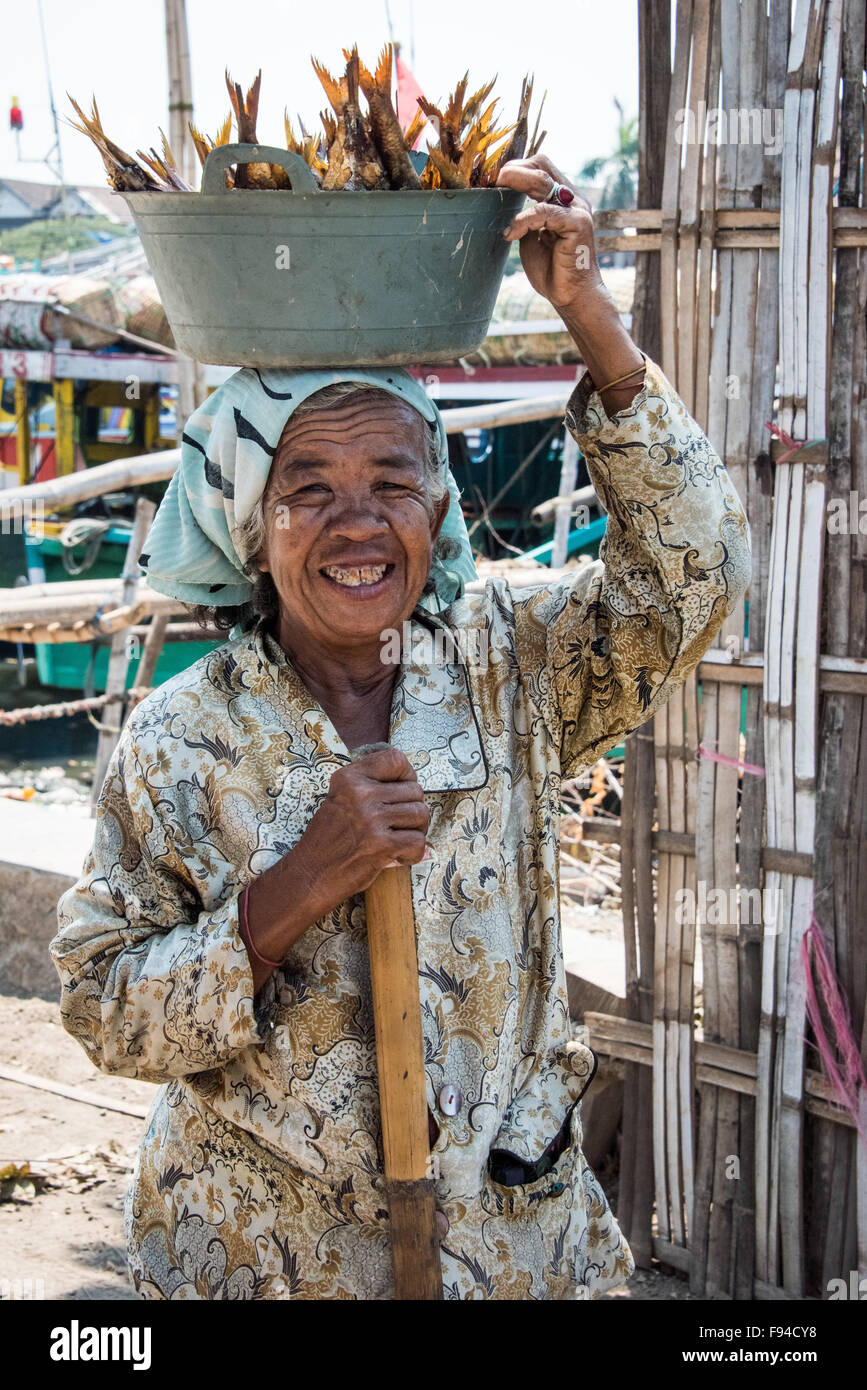 Dame transport du poisson dans le récipient sur la tête, Surabaya, Indonésie Banque D'Images