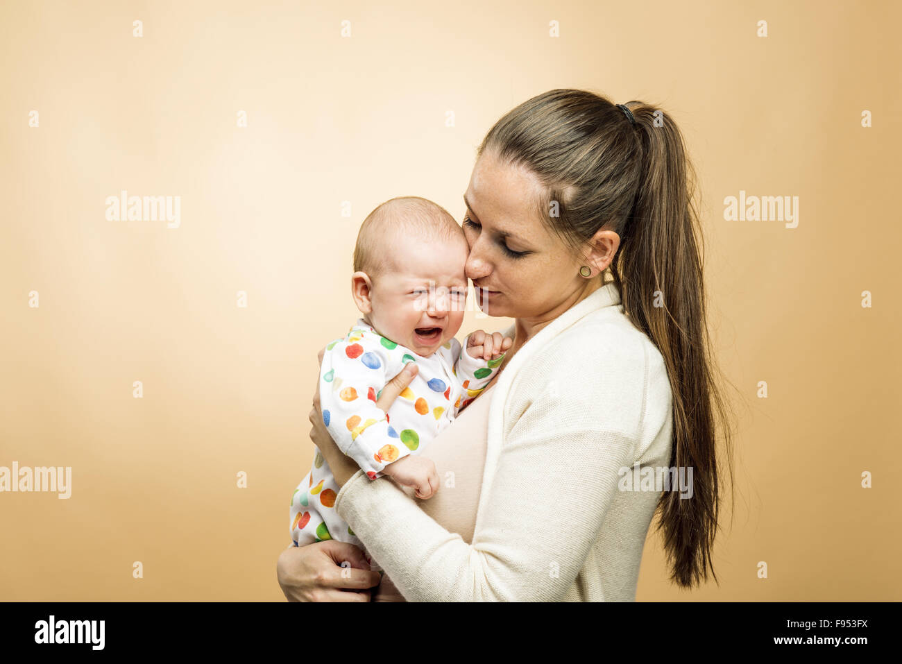 Enfant pleurant avec mère studio shot sur fond beige Banque D'Images