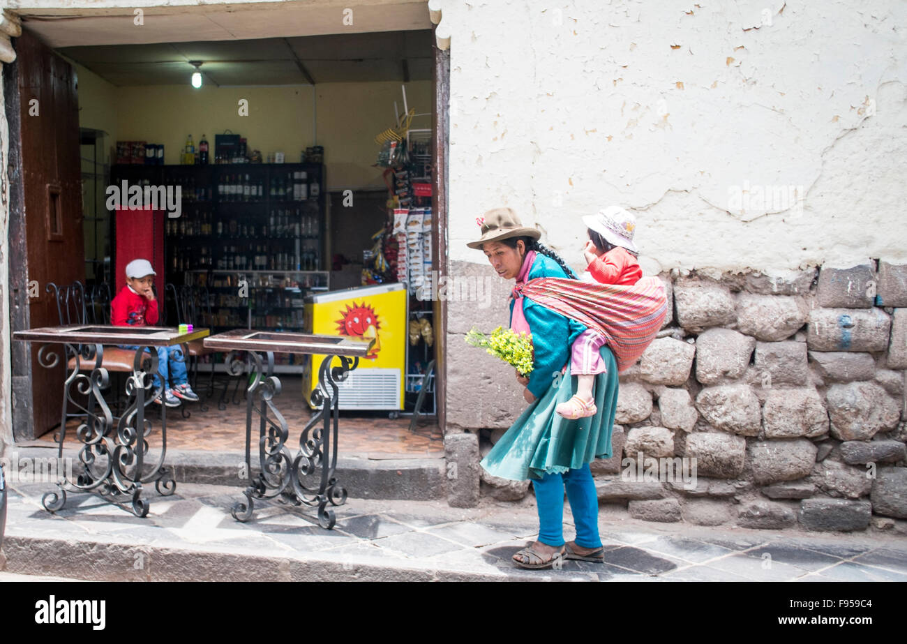Cusco, Pérou. Une femme porte son enfant tout en marchant le long d'une rue . Banque D'Images