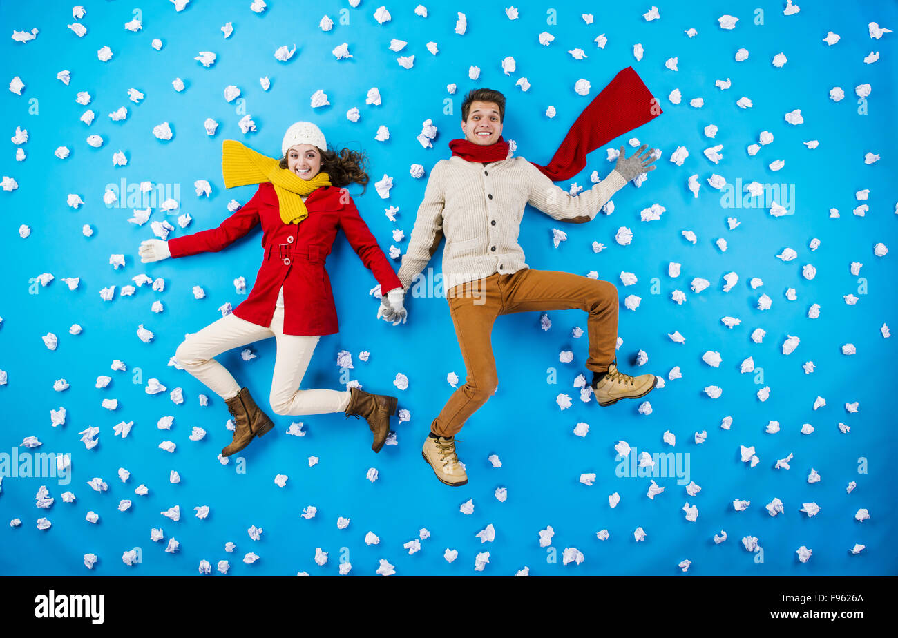 Happy young couplein les vêtements d'hiver s'amusant contre le fond bleu avec des flocons Banque D'Images