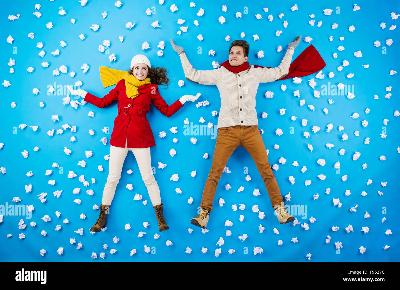 Happy young couplein les vêtements d'hiver s'amusant contre le fond bleu avec des flocons Banque D'Images