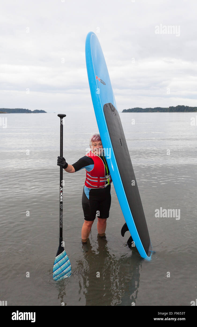 A senior woman vient à terre avec son stand up paddle board pagaie après dans les eaux au large de la plage Histoires près de Port Hardy Banque D'Images