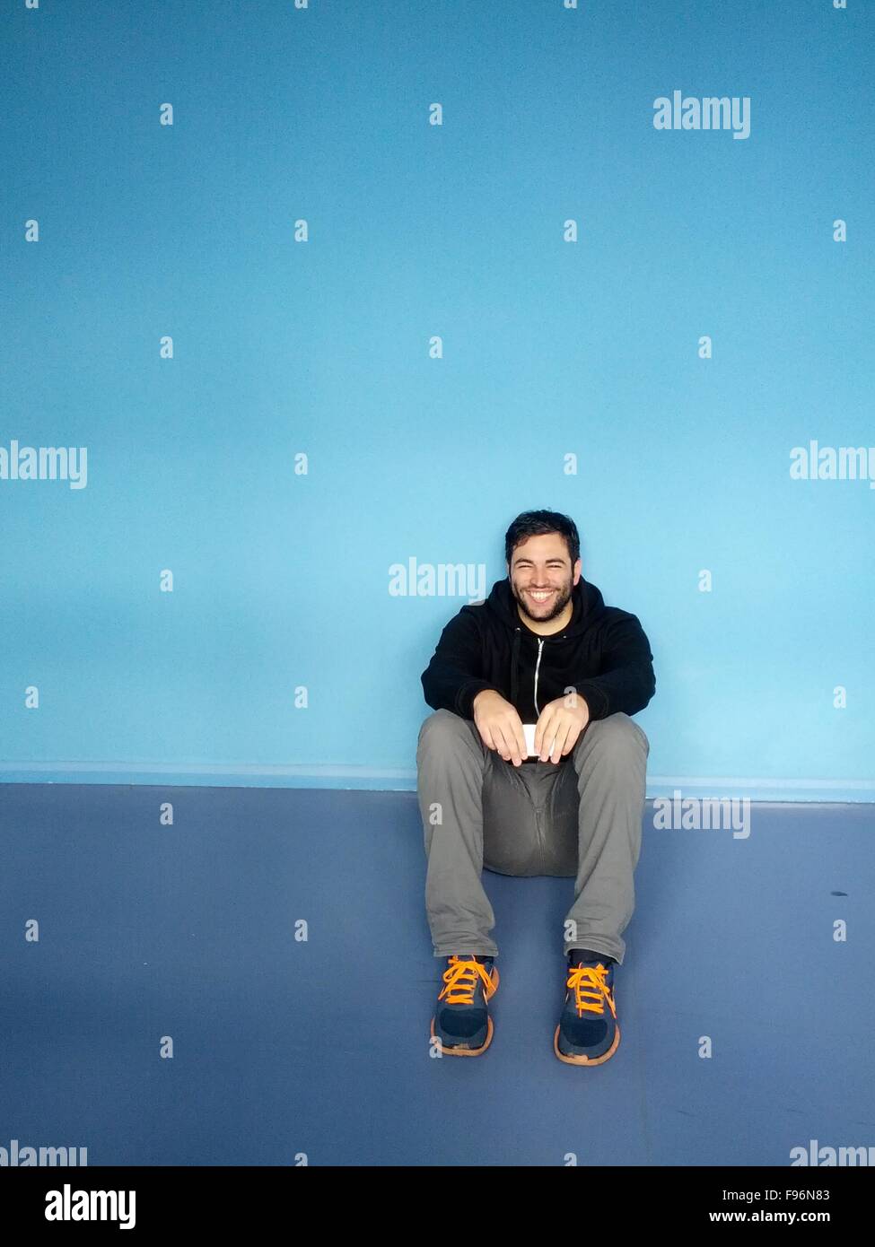 Portrait Of A Smiling Young Man Sitting contre mur bleu Banque D'Images