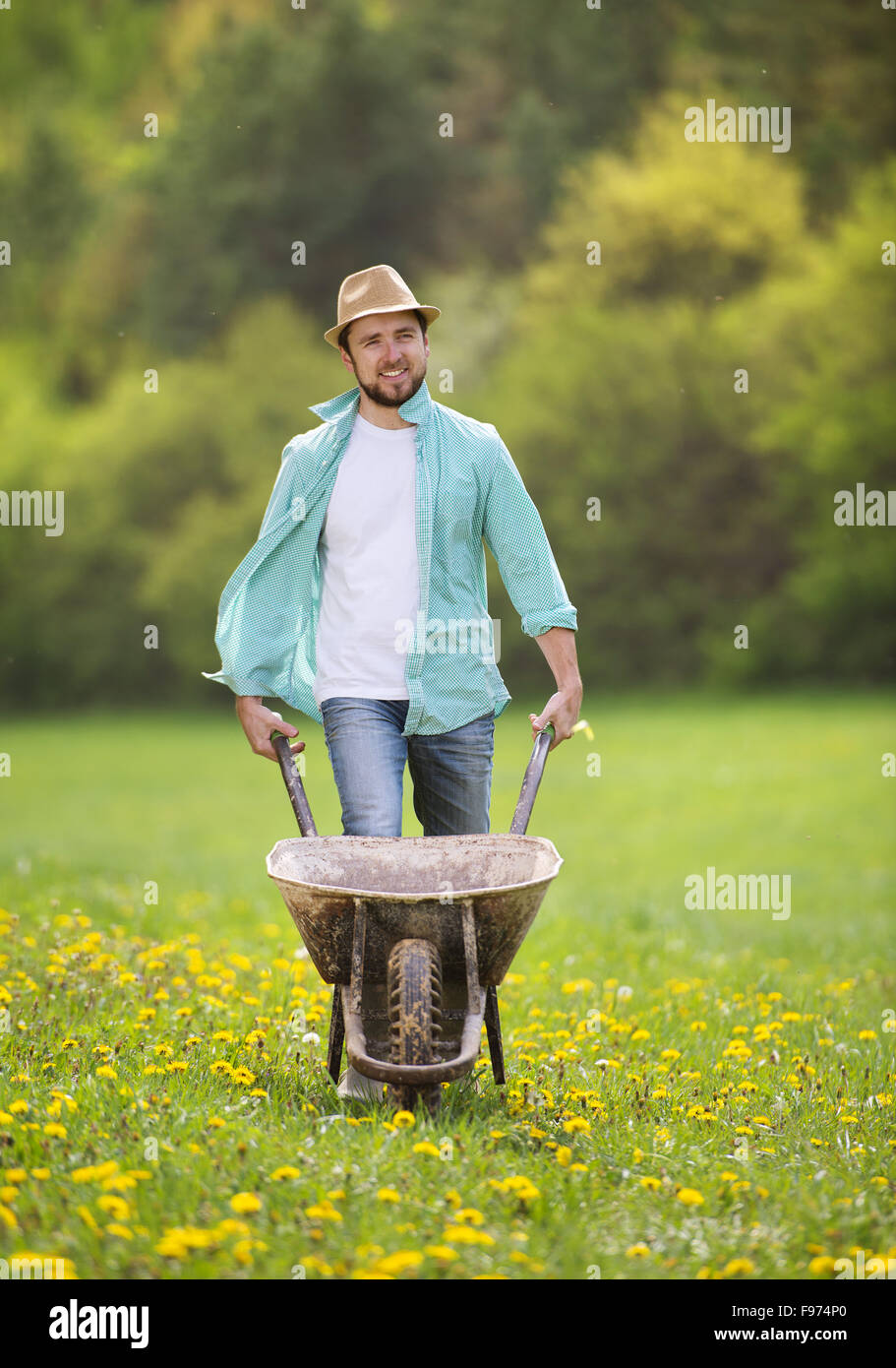 Jeune agriculteur pushing wheelbarrow dans le domaine Banque D'Images