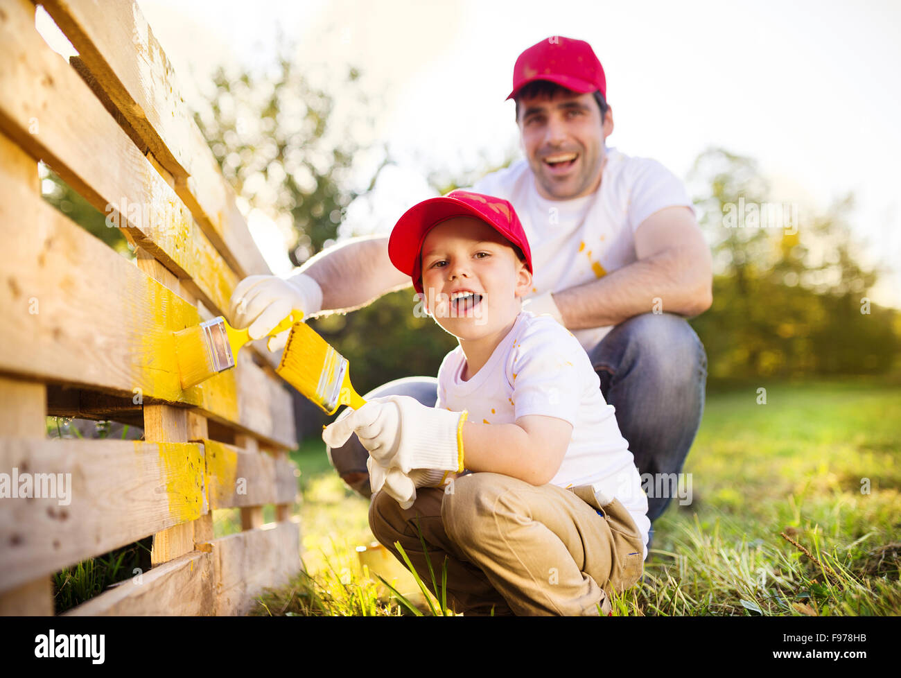 Adorable petit garçon et de son père dans la peinture red caps clôture en bois ensemble sur journée ensoleillée dans la nature Banque D'Images