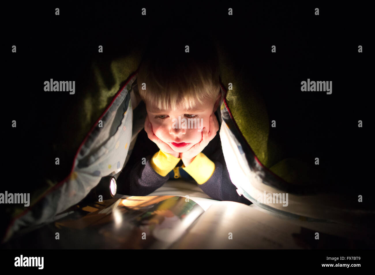 Garçon de 5 ans la lecture d'un livre à la lumière de torches sous sa couette la nuit, England, UK Banque D'Images