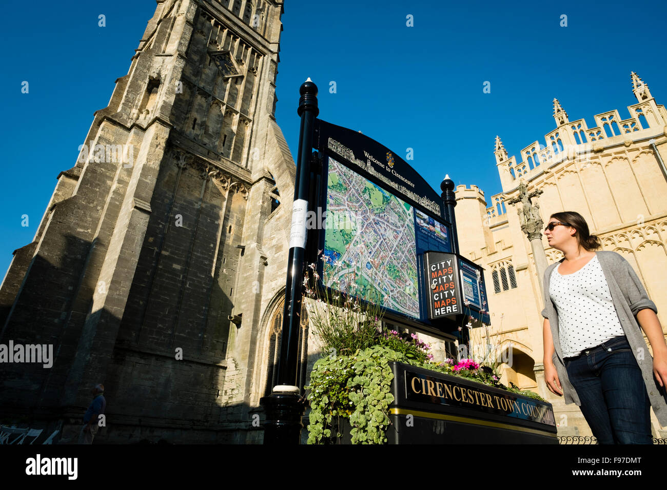 Une femme à la recherche à un site d'information touristique à l'extérieur de l'église de Saint-Jean-Baptiste , église paroissiale dans l'Église d'Angleterre à Cirencester, Gloucestershire, England, UK Banque D'Images