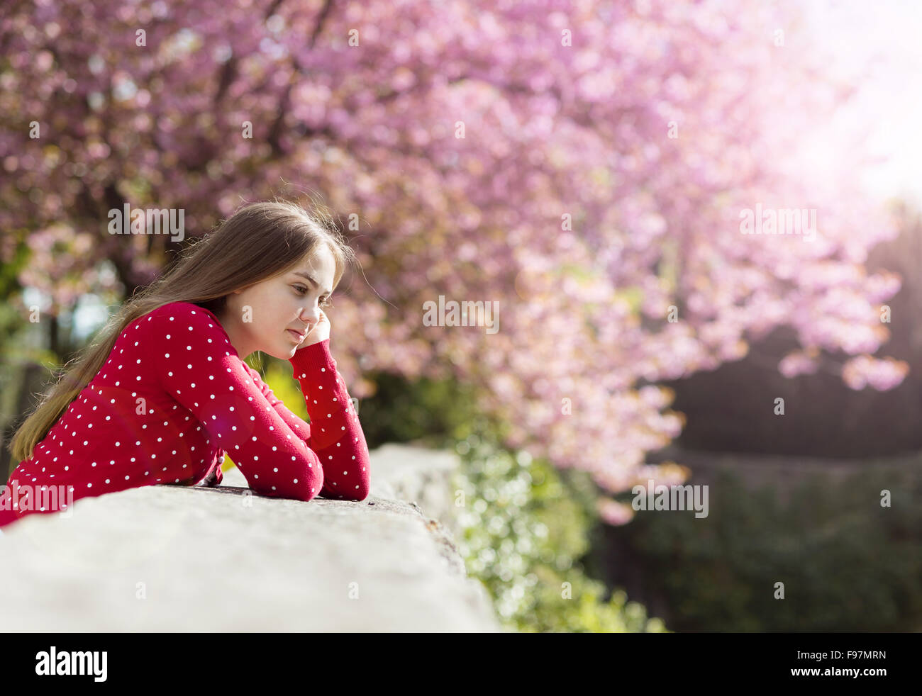 Belle fille de cardigan rouge gisant au printemps relaxant jardin avec arbres en fleurs Banque D'Images