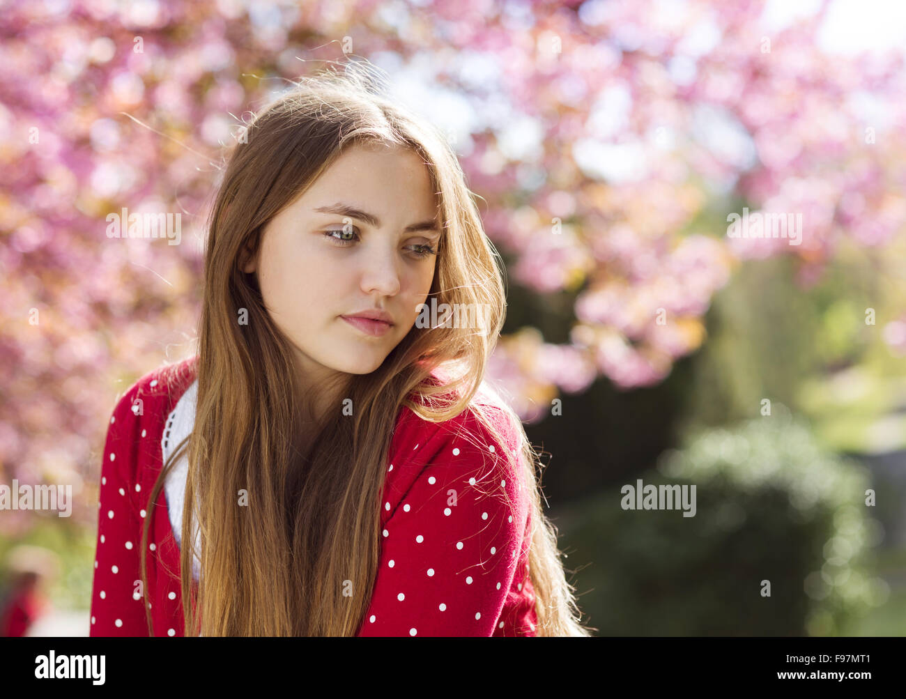 Belle fille de cardigan rouge gisant au printemps relaxant jardin avec arbres en fleurs Banque D'Images