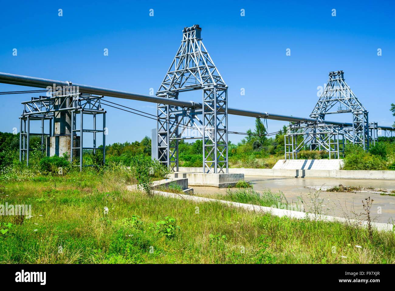 Les lignes de conduite de gaz qui a jeté à travers la rivière boueuse et forêt vert paysage en été, la Roumanie. Banque D'Images