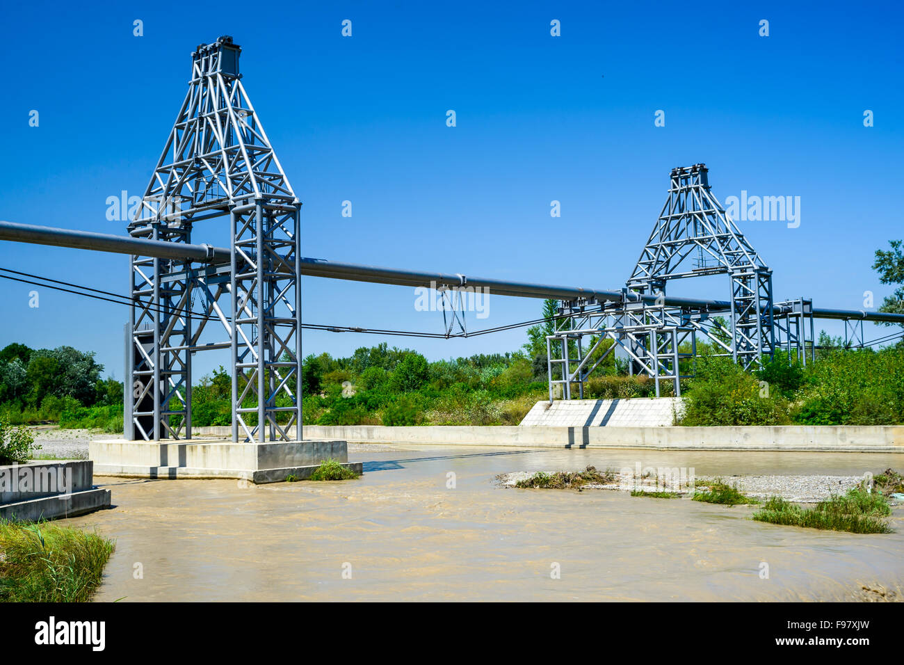 Les lignes de conduite de gaz qui a jeté à travers la rivière boueuse et forêt vert paysage en été, la Roumanie. Banque D'Images