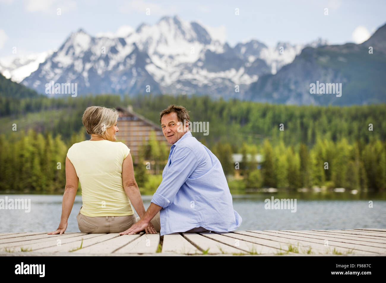 Senior couple sitting on pier au-dessus du lac de montagne avec des montagnes en arrière-plan Banque D'Images