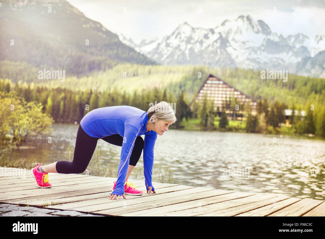 Senior woman se prépare le jogging autour du tarn en belles montagnes, collines et hôtel en arrière-plan Banque D'Images