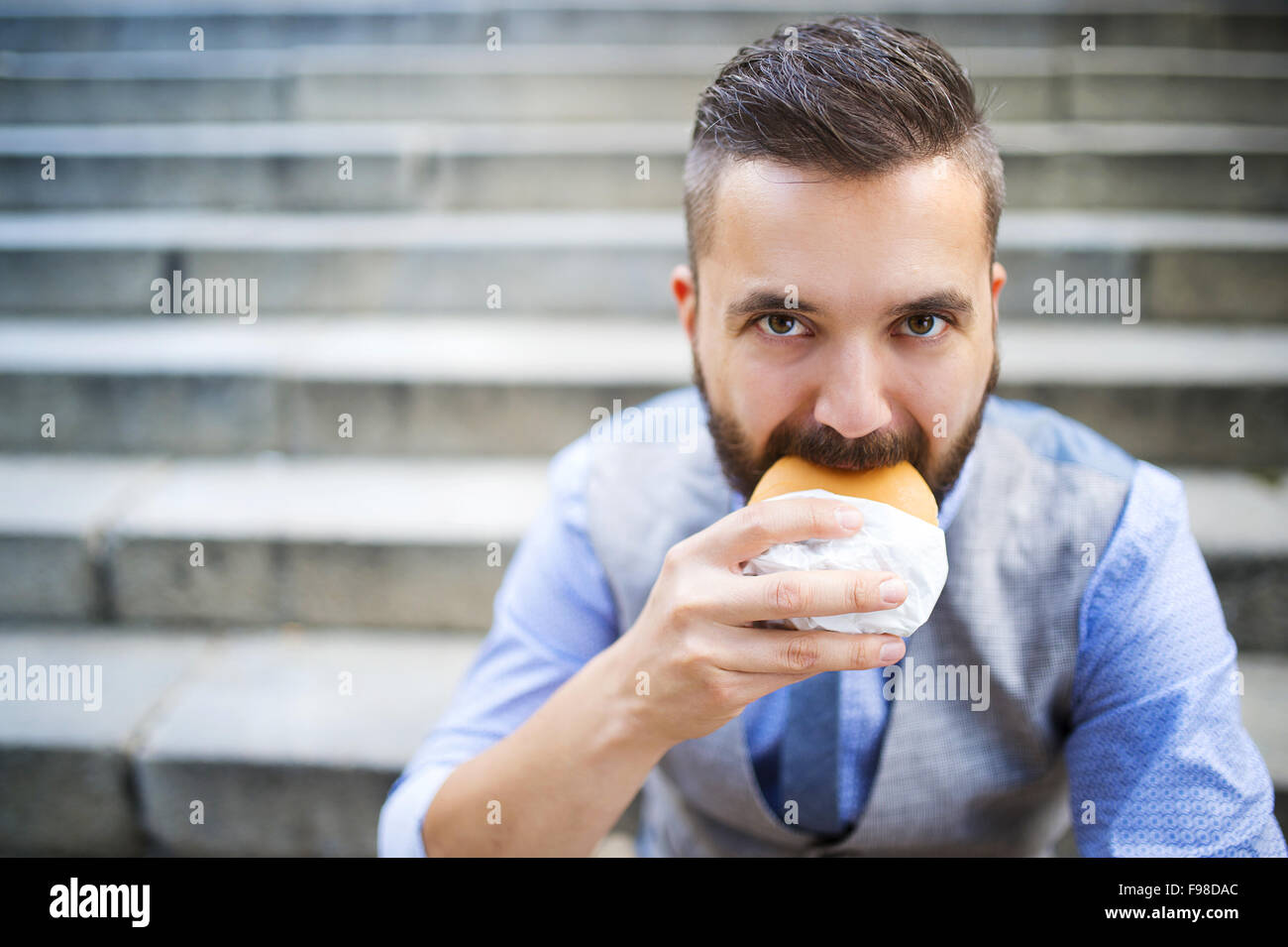 Hipster moderne businessman having lunch break, assis sur des escaliers en centre-ville et de manger burger Banque D'Images