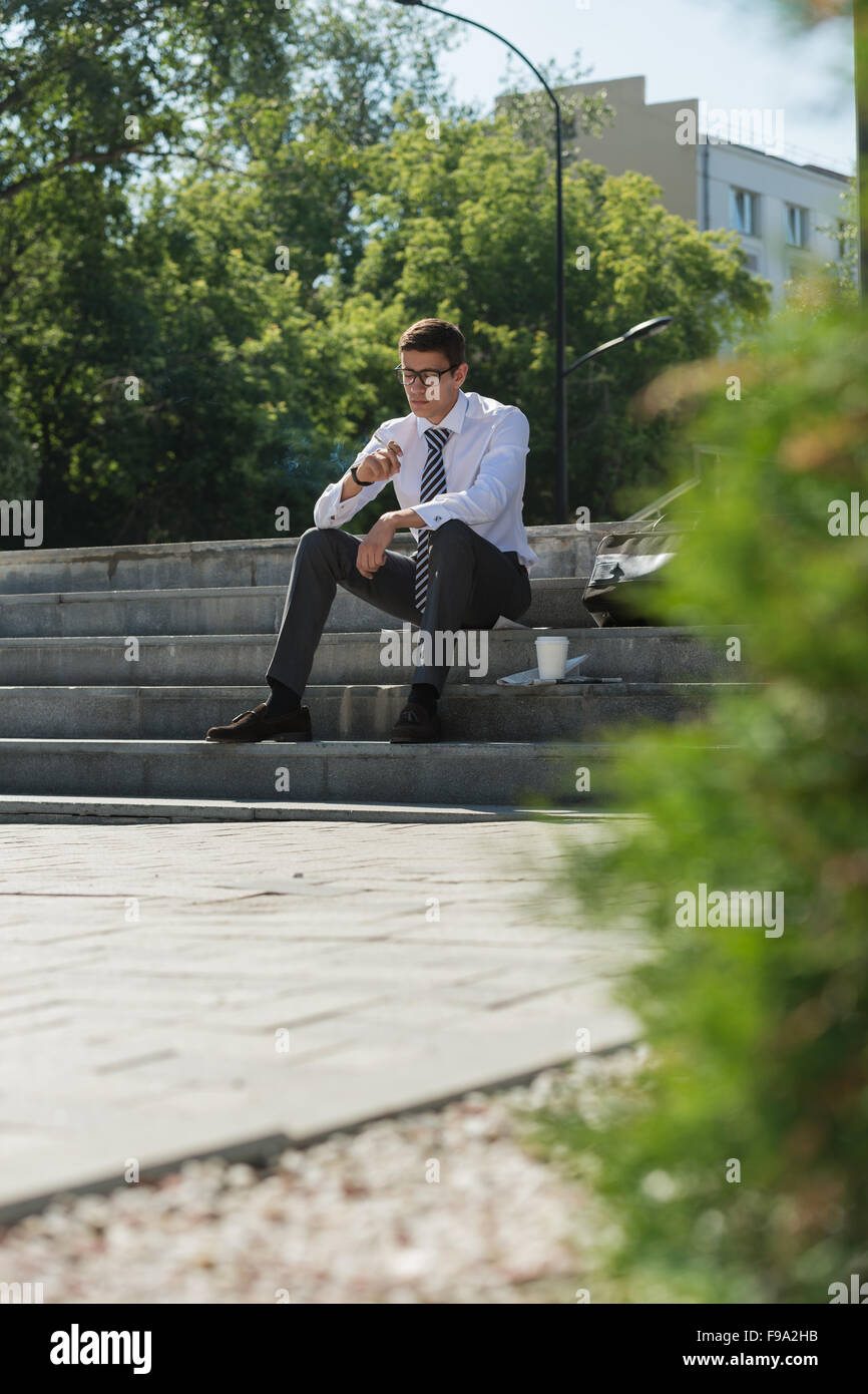 L'homme d'affaires bien habillés fumeur assis sur un trottoir de la rue Banque D'Images