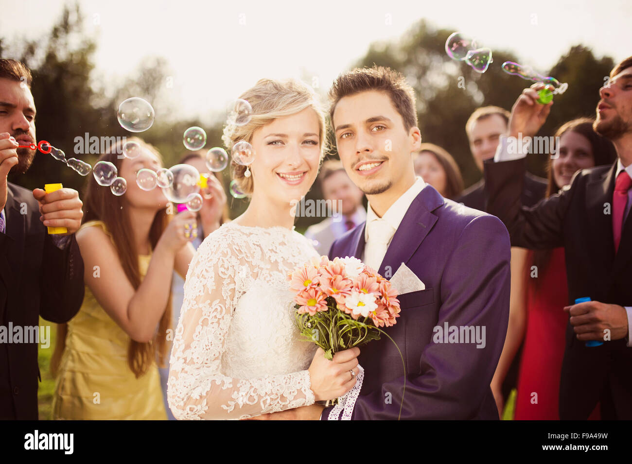 Les jeunes mariés profiter de moment romantique ensemble à réception de mariage à l'extérieur, les invités du mariage en arrière-plan blowing bubbles Banque D'Images