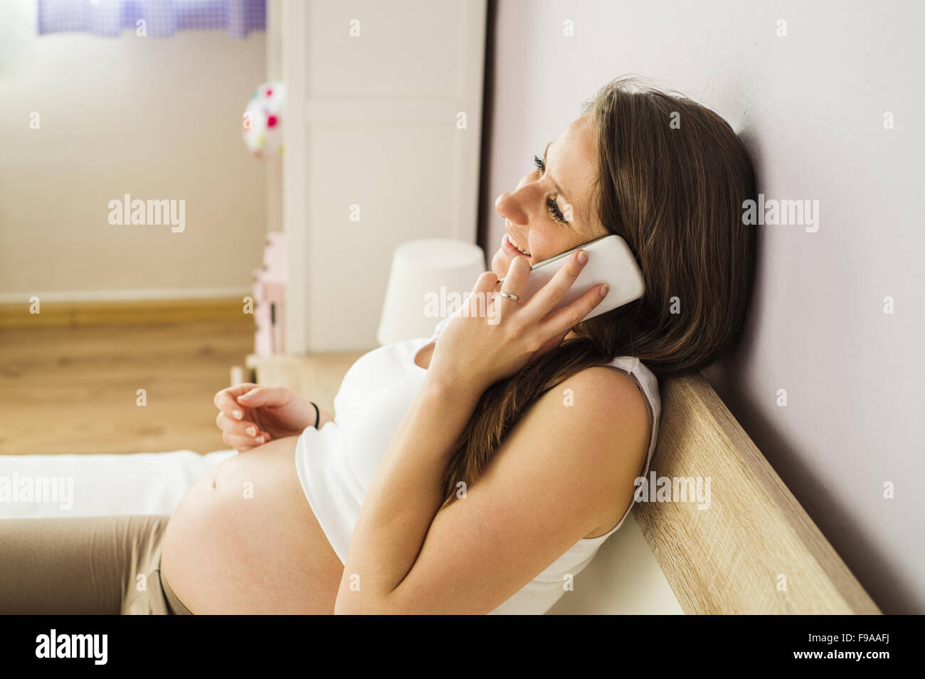 Beautiful pregnant woman talking on mobile phone dans sa chambre à coucher Banque D'Images