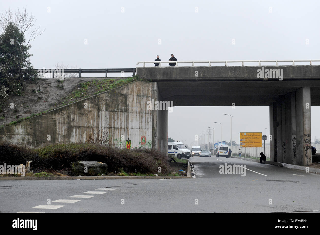 La Jungle, Calais, France. Les réfugiés et les migrants flâner par l'entrée du camp par l'autoroute gardé par des policiers Banque D'Images