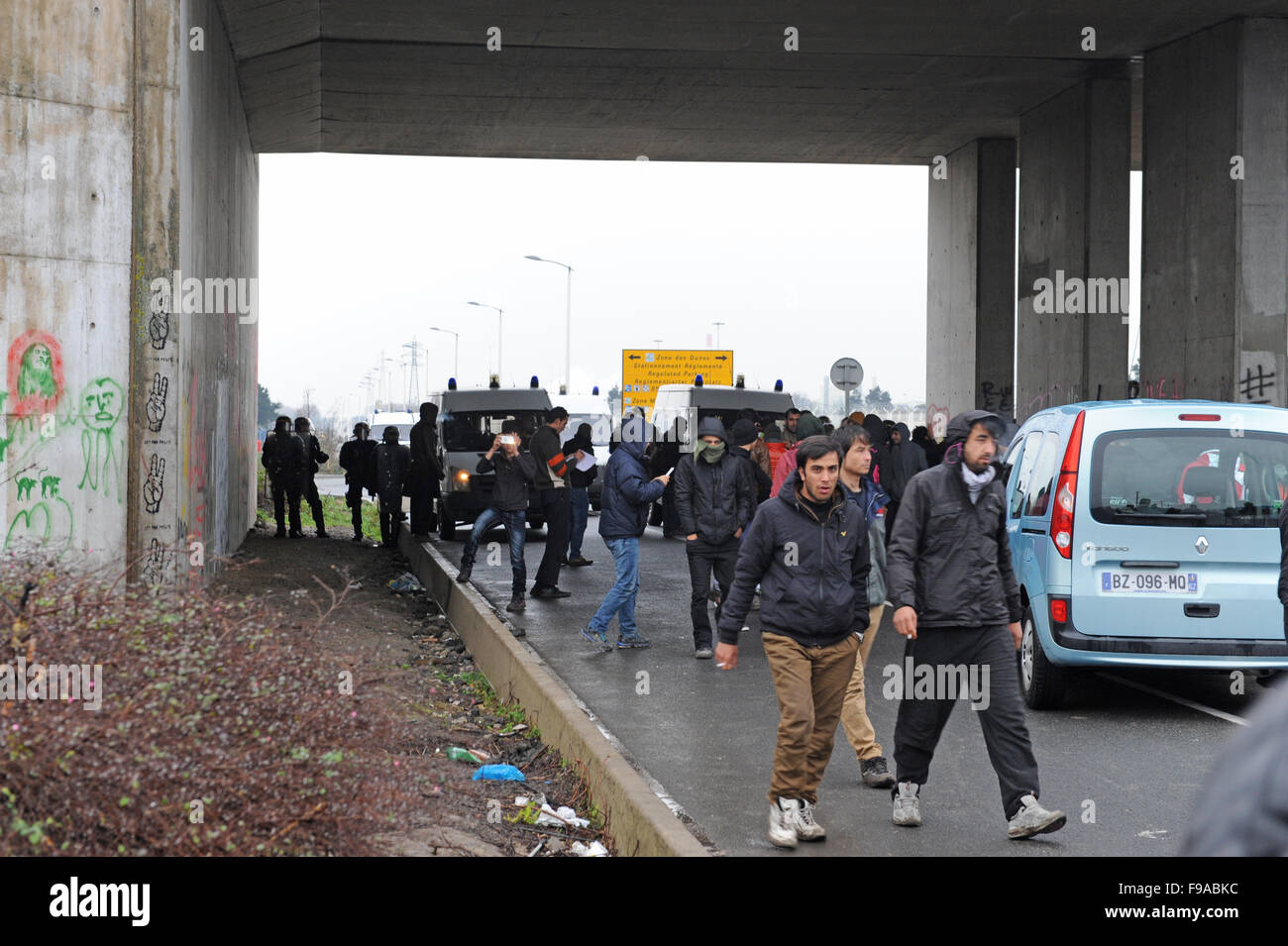 La Jungle, Calais, France. Les réfugiés et les migrants flâner par l'entrée du camp par l'autoroute gardé par des policiers Banque D'Images