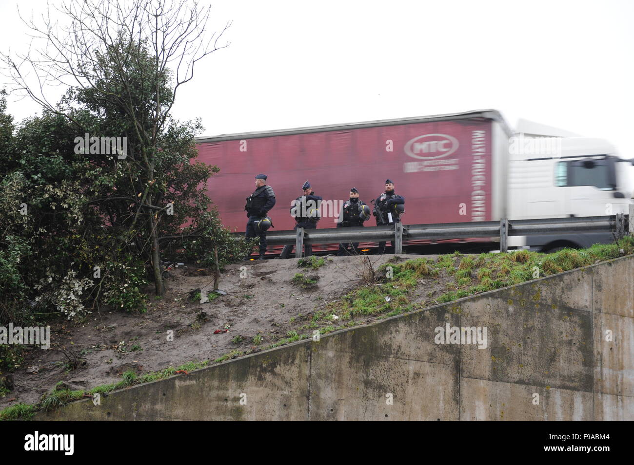 Jungle, Calais, France. Quatre policiers armés gardent l'autoroute à la sortie du camp comme un camion contenant des disques durs. Banque D'Images