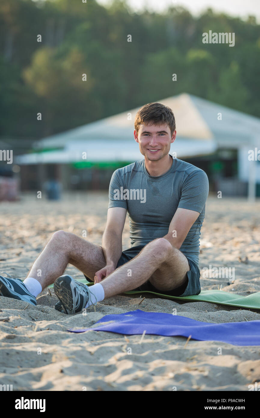 L'homme sportif après entraînement au repos sur la plage pendant le coucher du soleil Banque D'Images