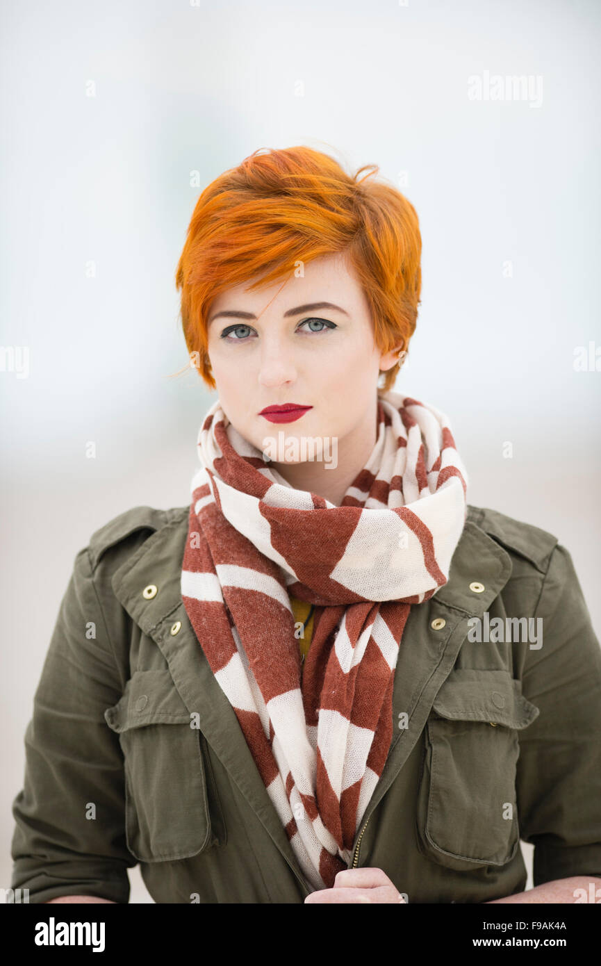 Un seul adolescent solo femme fille teint de peau pâle et rouge flamme  coupe courte cheveux courts portant un manteau veste verte et un foulard ,  par elle-même, à l'extérieur, UK Photo