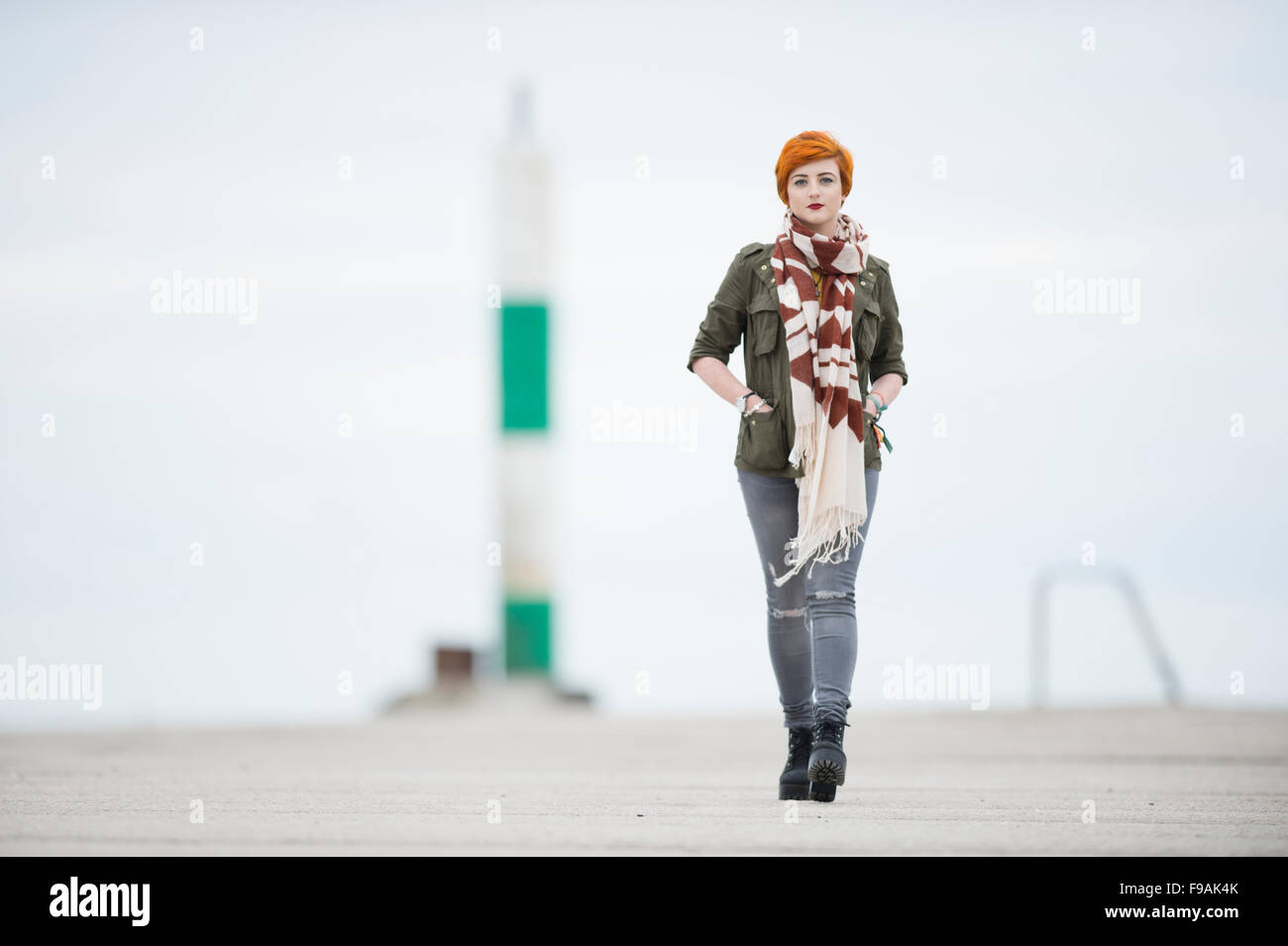Un seul adolescent solo femme fille teint de peau pâle et rouge flamme cheveux courts portant un manteau veste verte et un foulard , marcher marcher par elle-même, à l'extérieur, UK Banque D'Images