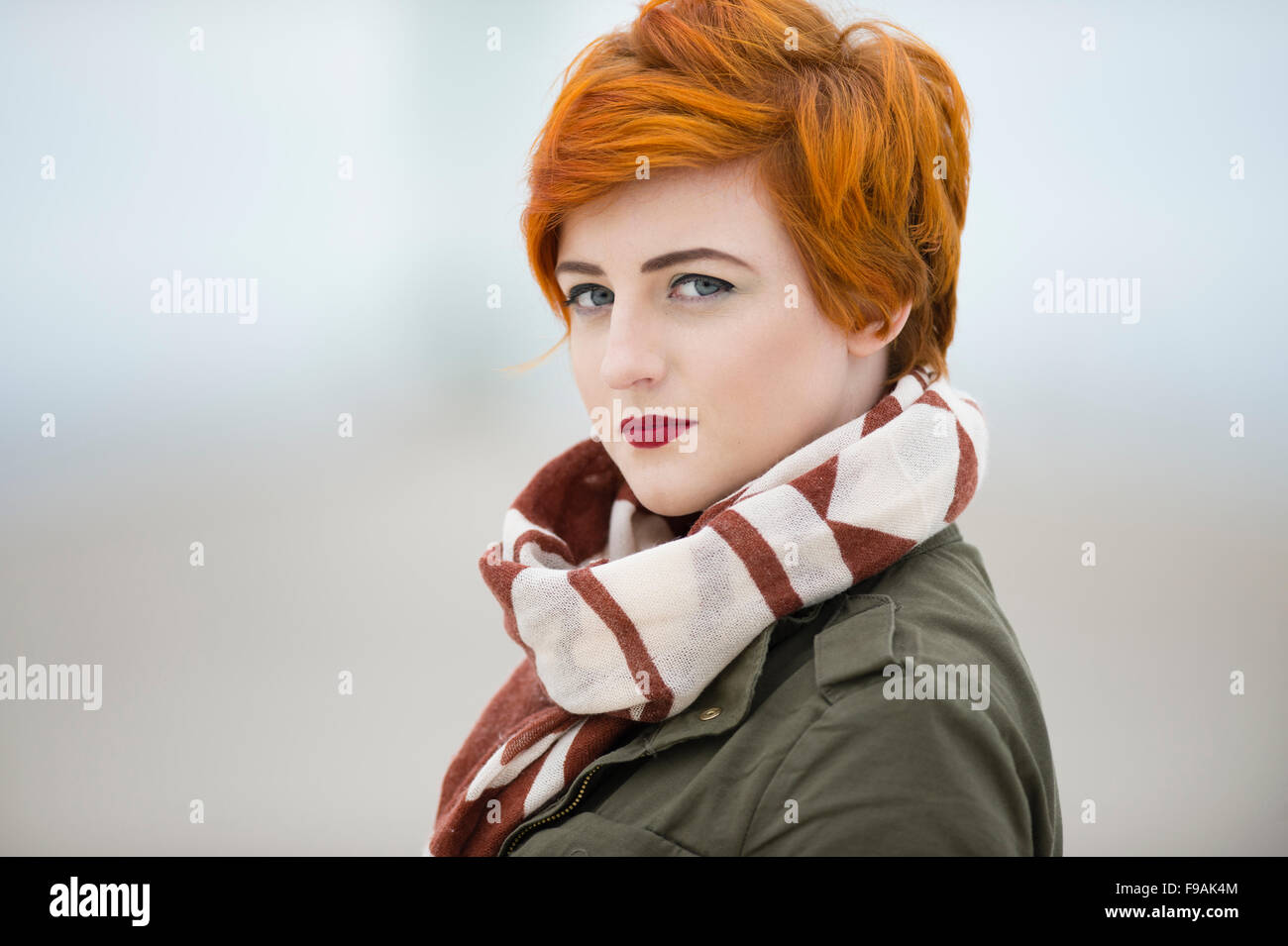 Un seul adolescent solo femme fille teint de peau pâle et rouge flamme  cheveux courts portant un manteau veste verte et un foulard , par  elle-même, à l'extérieur, UK Photo Stock -