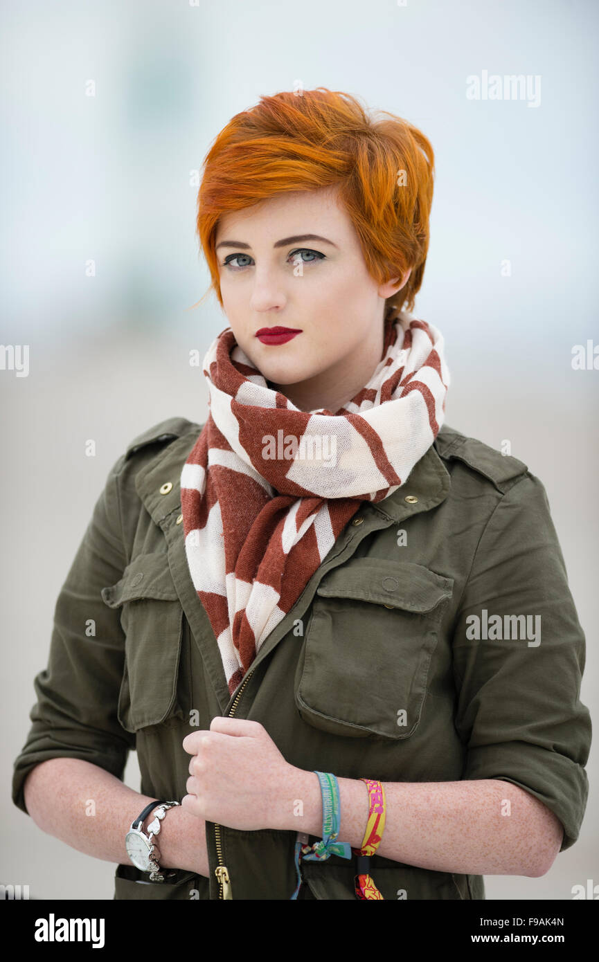 Un seul adolescent solo femme fille teint de peau pâle et rouge flamme cheveux courts portant un manteau veste verte et un foulard , par elle-même, à l'extérieur, UK Banque D'Images