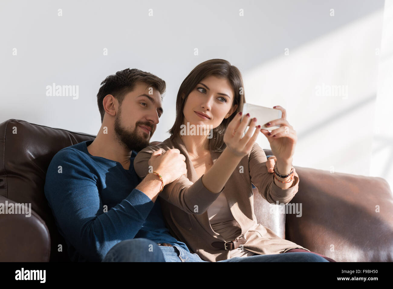 Cheerful couple prendre une avec un smartphone selfies at home sitting on couch Banque D'Images