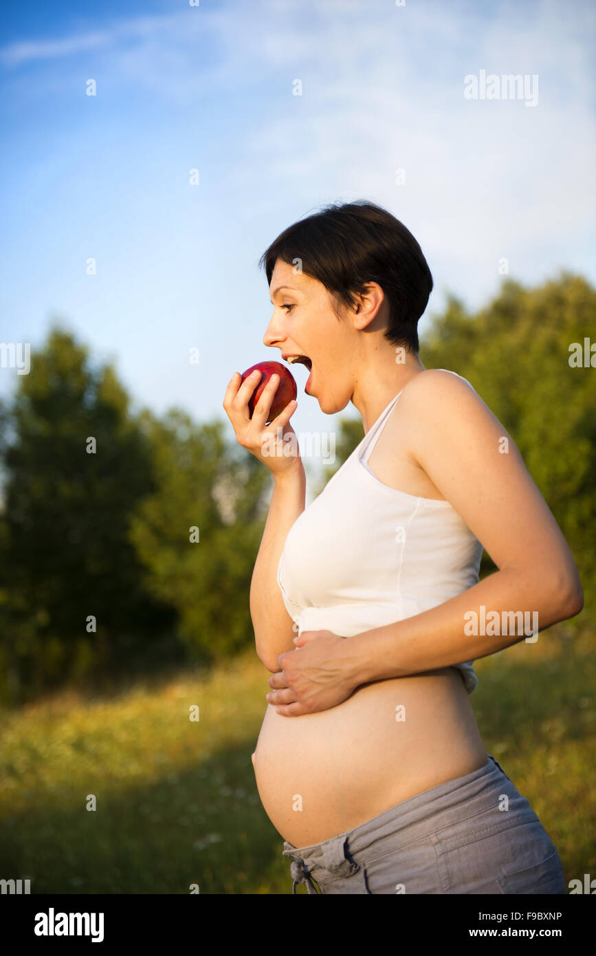 Portrait of young pregnant woman eating apple en nature Banque D'Images