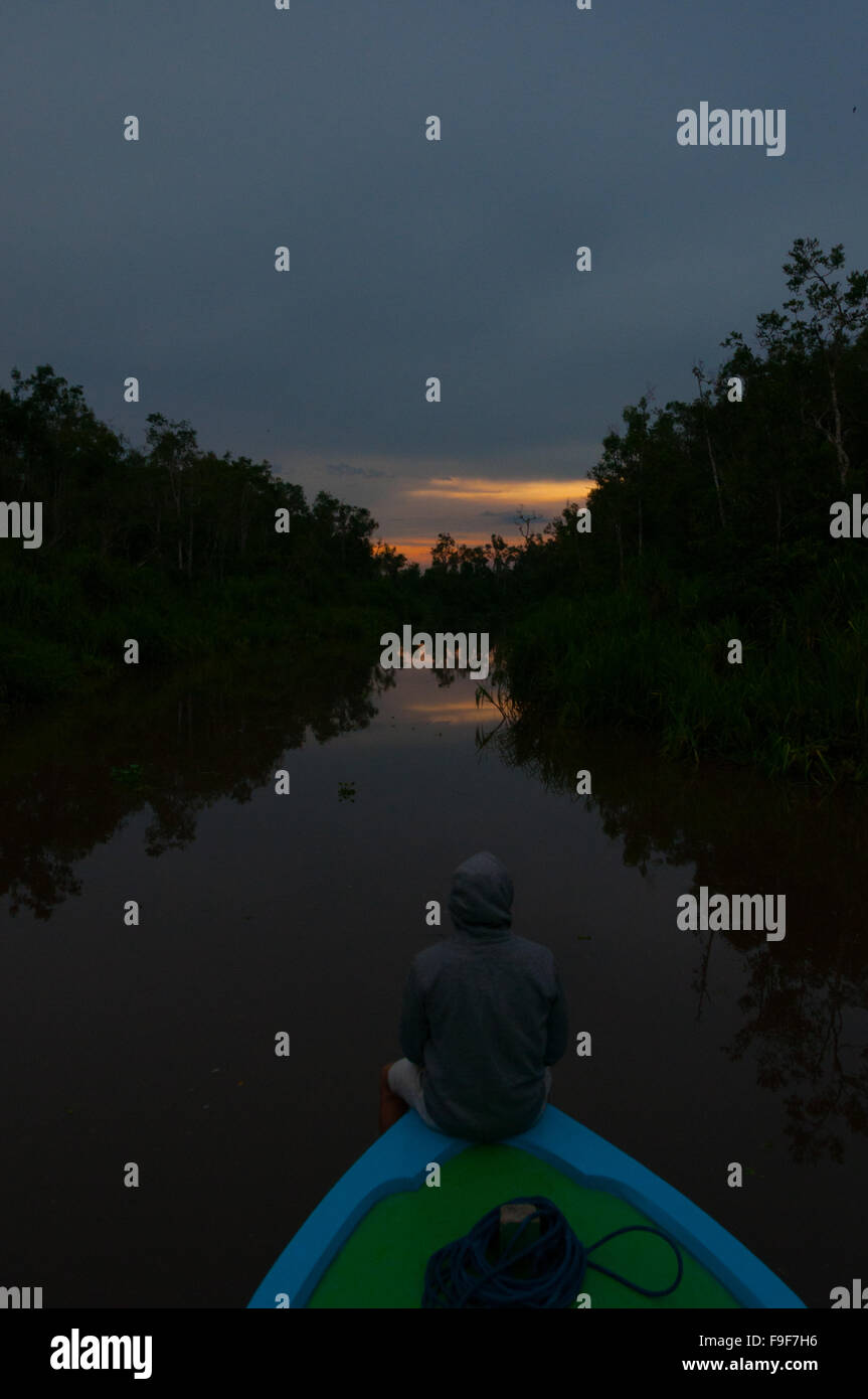 Personne assise en face d'un bateau sur la rivière au coucher du soleil Banque D'Images